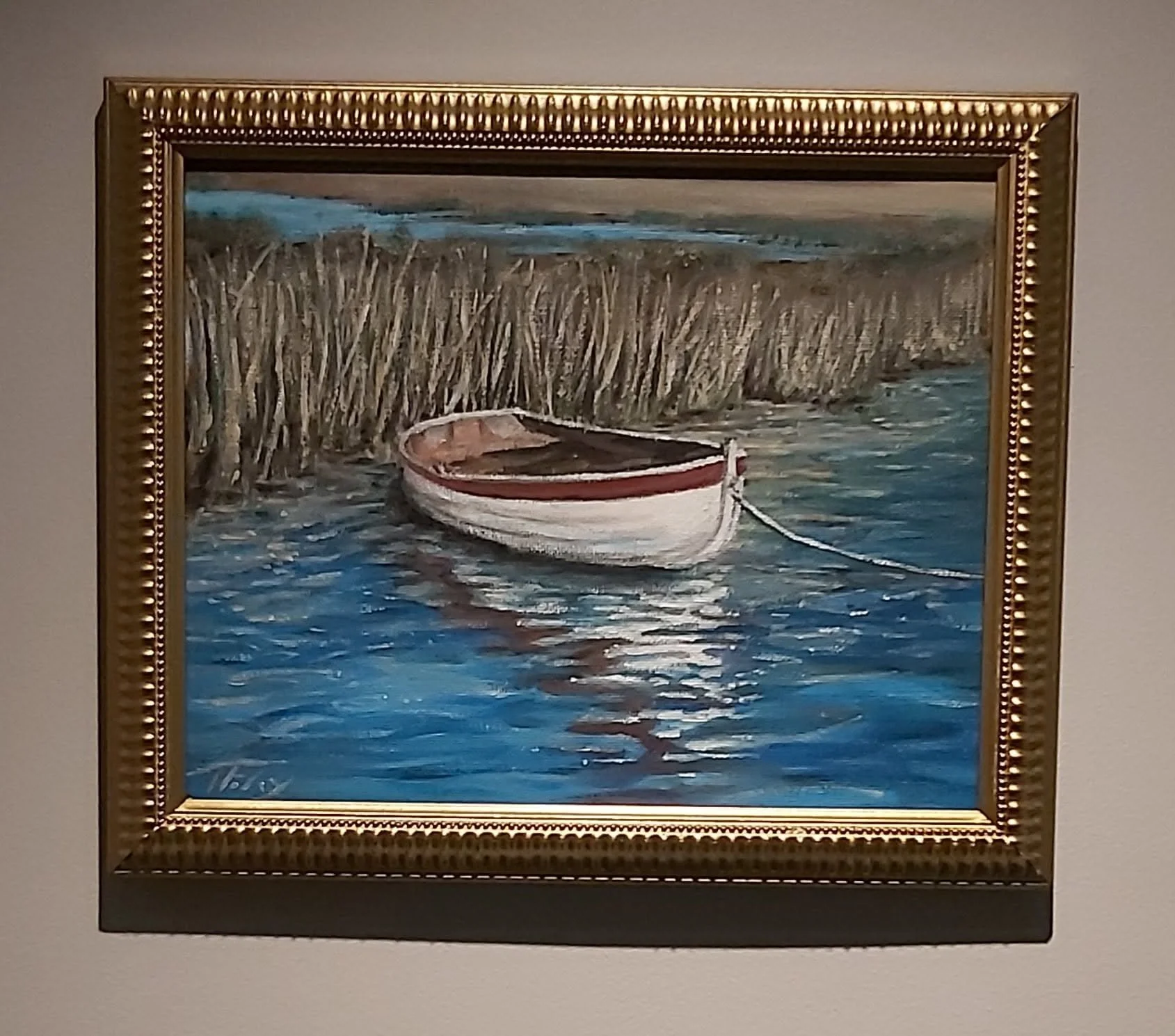 A framed painting of a small boat floating on a body of water near a grassy shoreline with reeds, under a cloudy sky.