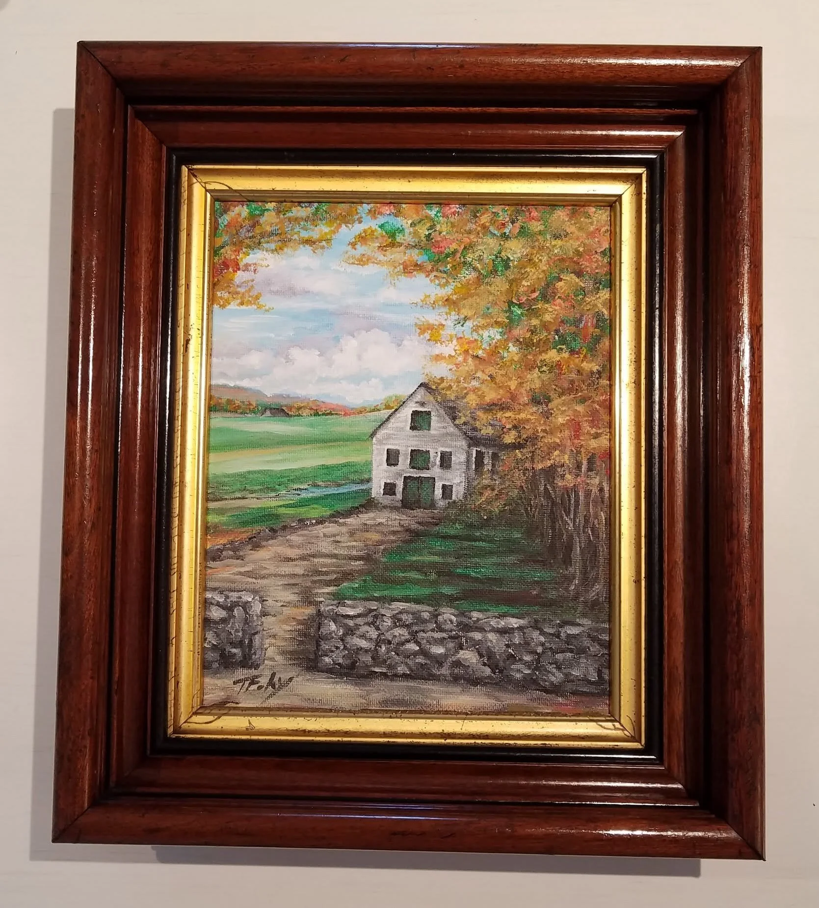 A framed landscape painting of a house with an autumn background, green fields, and a cloudy sky.