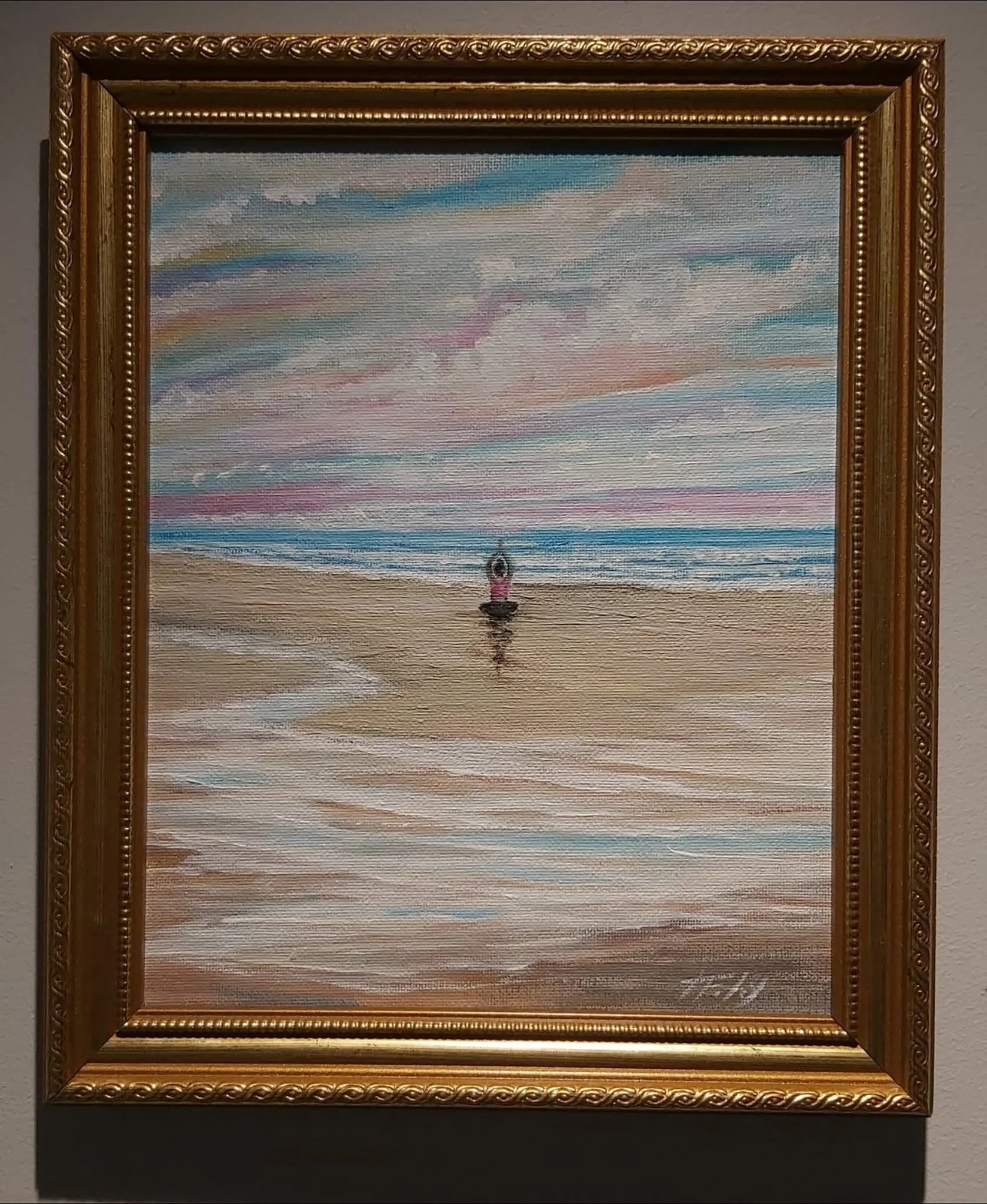 Painting of a sunset or sunrise over a calm body of water with colorful clouds and a small boat at the bottom center, framed in an ornate gold frame.