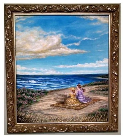 A framed painting of a woman in a purple dress sitting on a beach, with a dog beside her, overlooking the ocean under a blue sky with clouds.