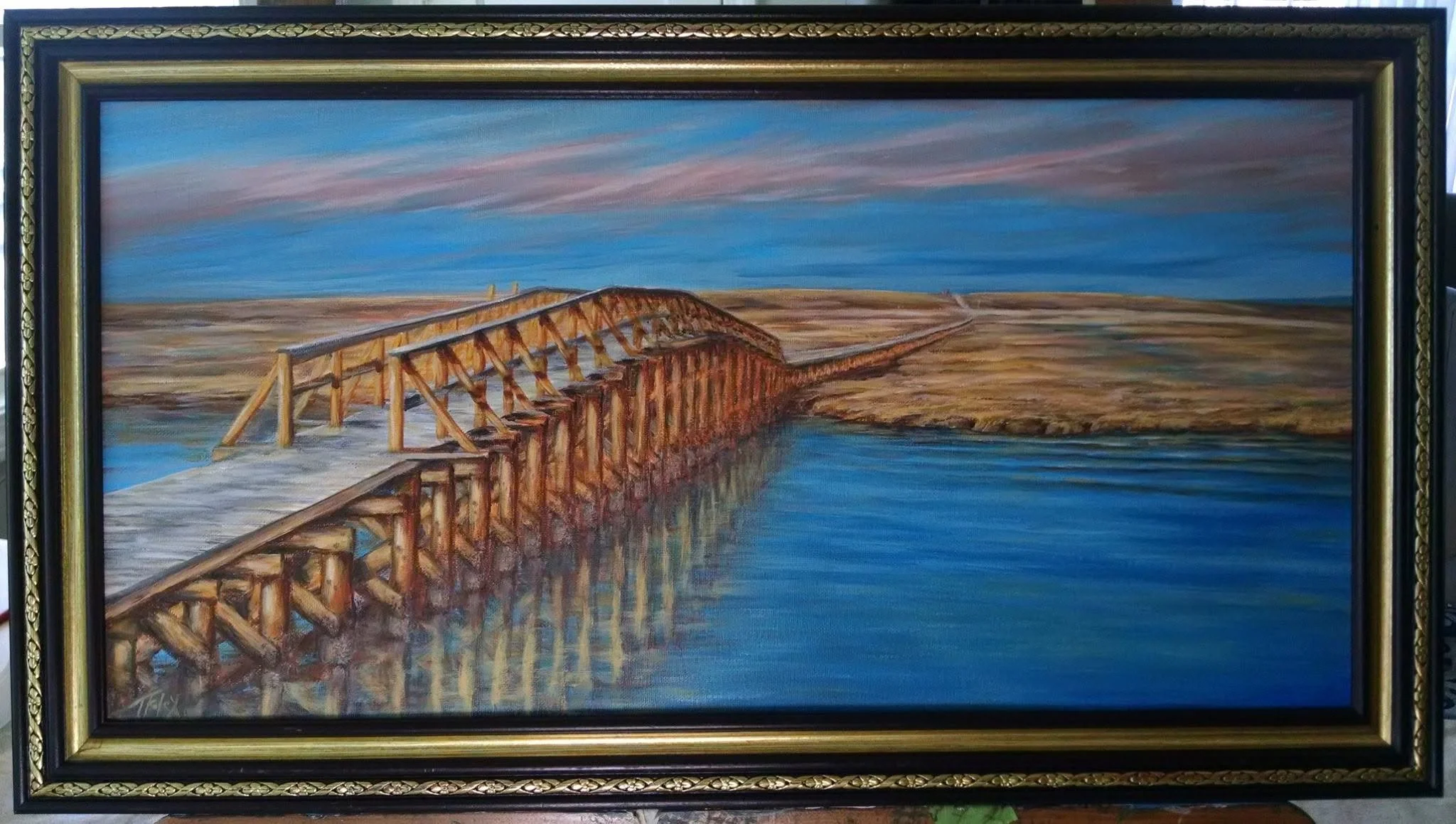 A framed painting of a wooden bridge over a body of water with a landscape of flat terrain and a partly cloudy sky.