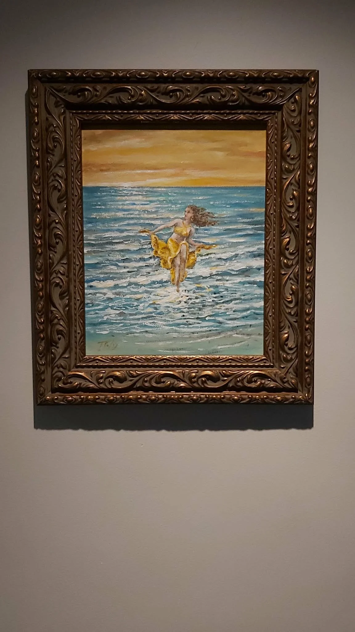 Painting of a woman in a yellow dress sitting on the ocean waves at sunset, framed in ornate wood.