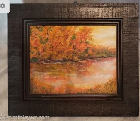 Landscape painting of a fall scene with colorful trees, a river, and a sunset in a dark wooden frame.