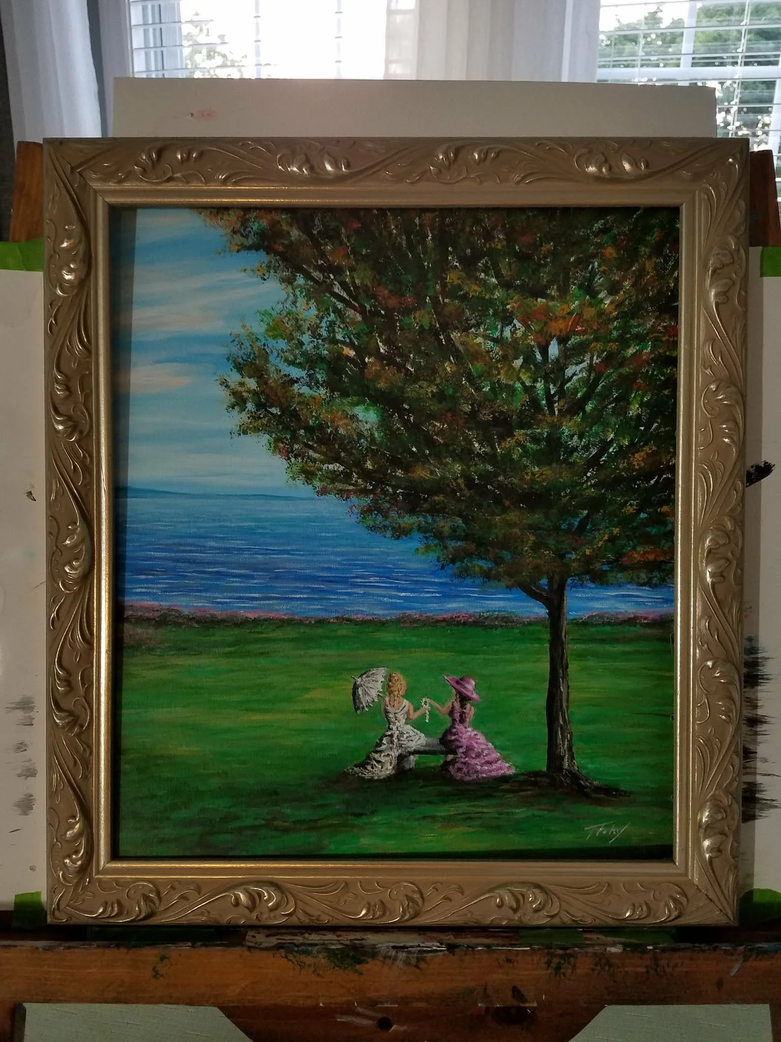 A painting of two women in vintage dresses sitting on grass beneath a large tree near a body of water, holding umbrellas and facing away from the viewer, with a colorful sky in the background.