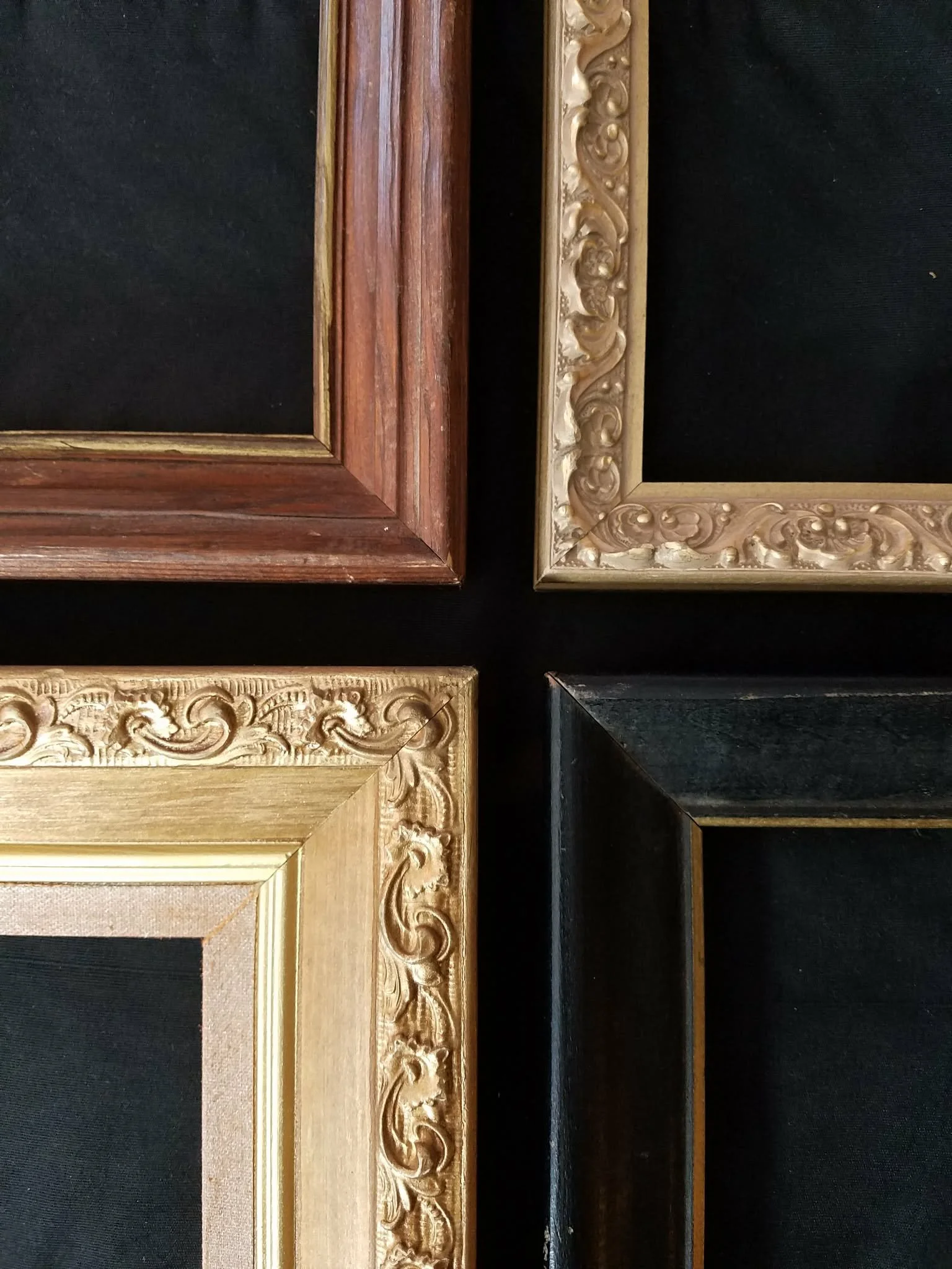 Four decorative picture frames laid flat on a black surface, each with a different ornate border design and color.