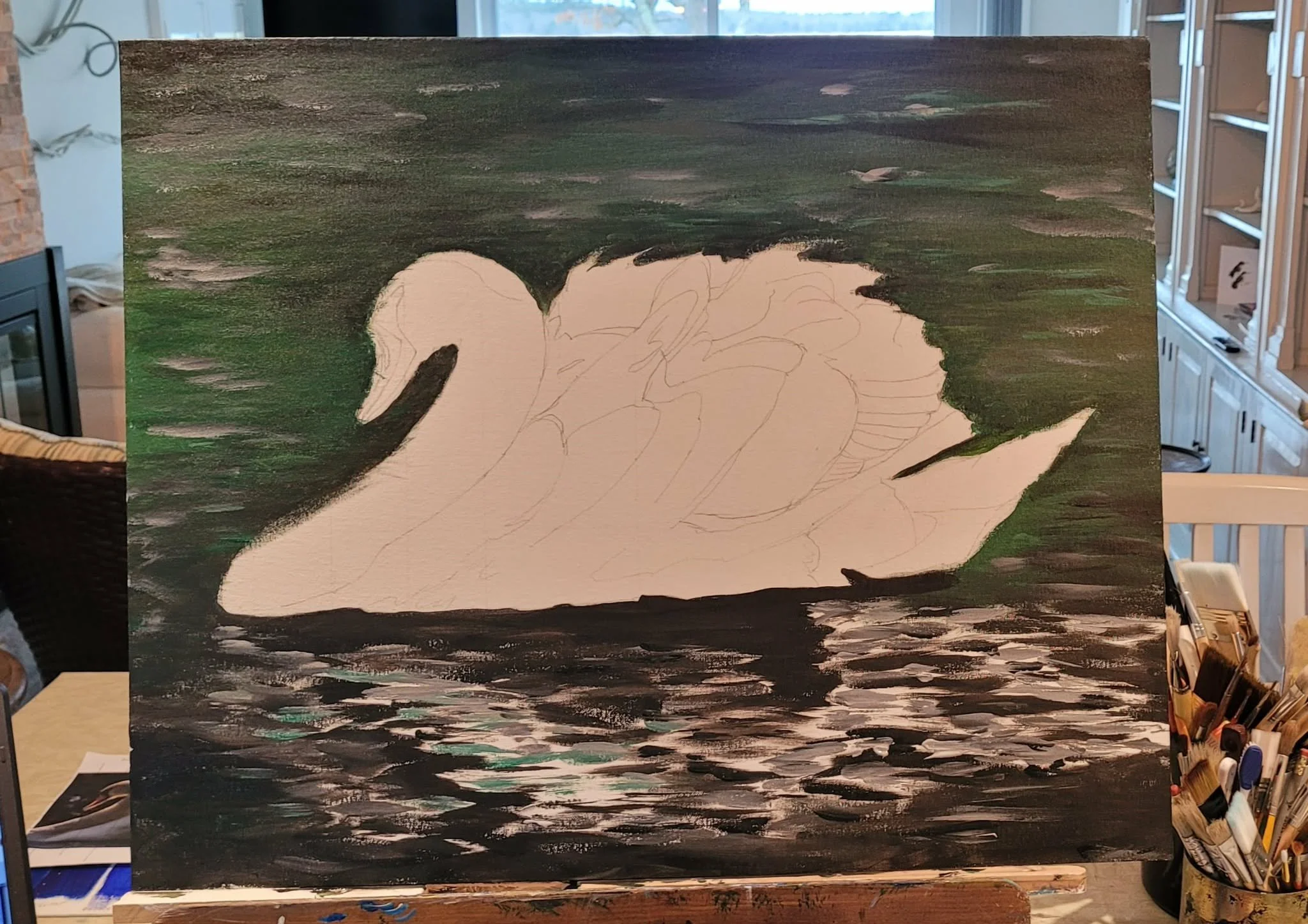 Unfinished painting of a swan on water, with a dark sky and landscape in the background, on an easel in an art studio.