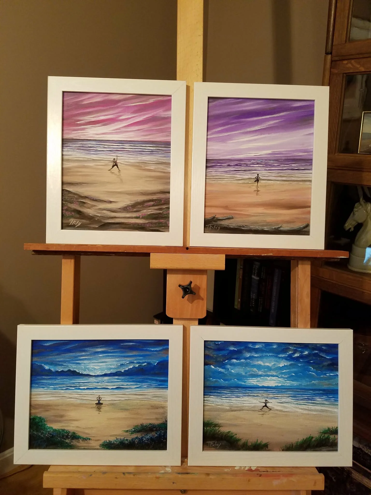Two framed landscape paintings of the beach with a person doing yoga, colorful sky with pink and purple hues