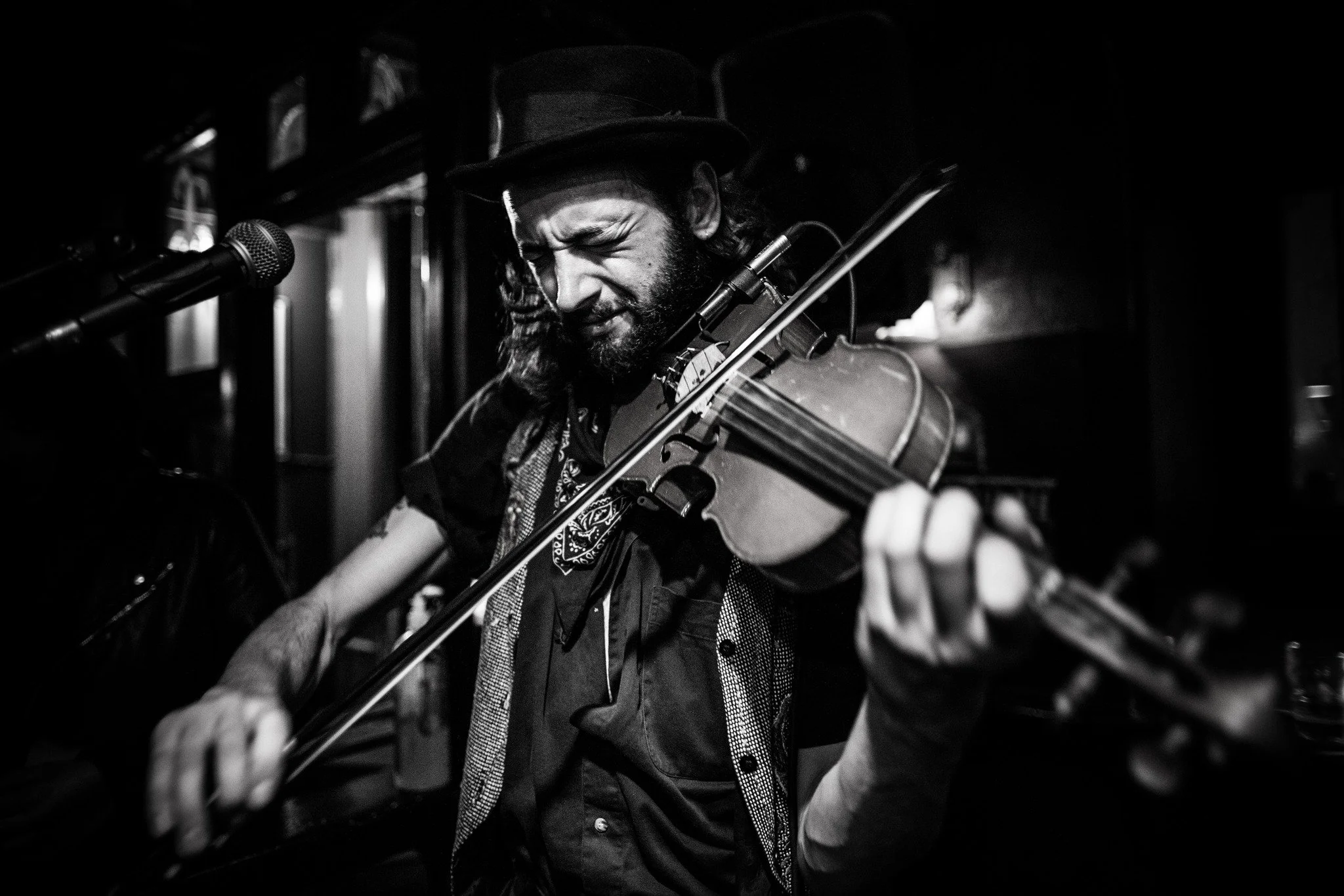 A man wearing a hat playing a violin, in a dark setting.