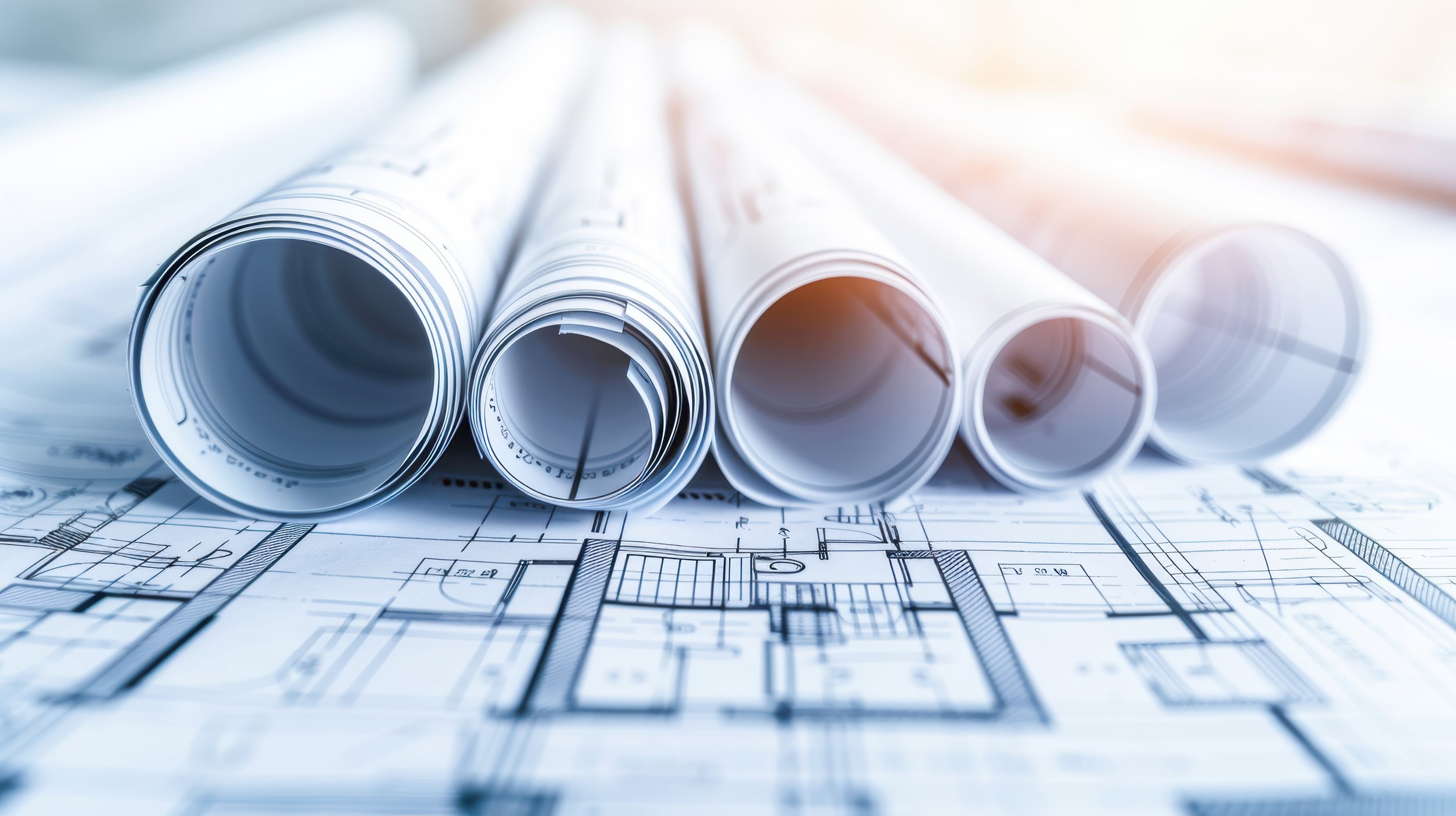 Stacked rolled blueprints on top of architectural plans with technical drawings.