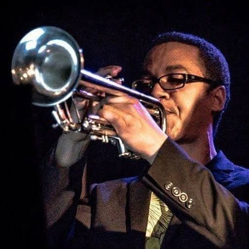 Musician playing a silver trumpet on stage under dramatic lighting
