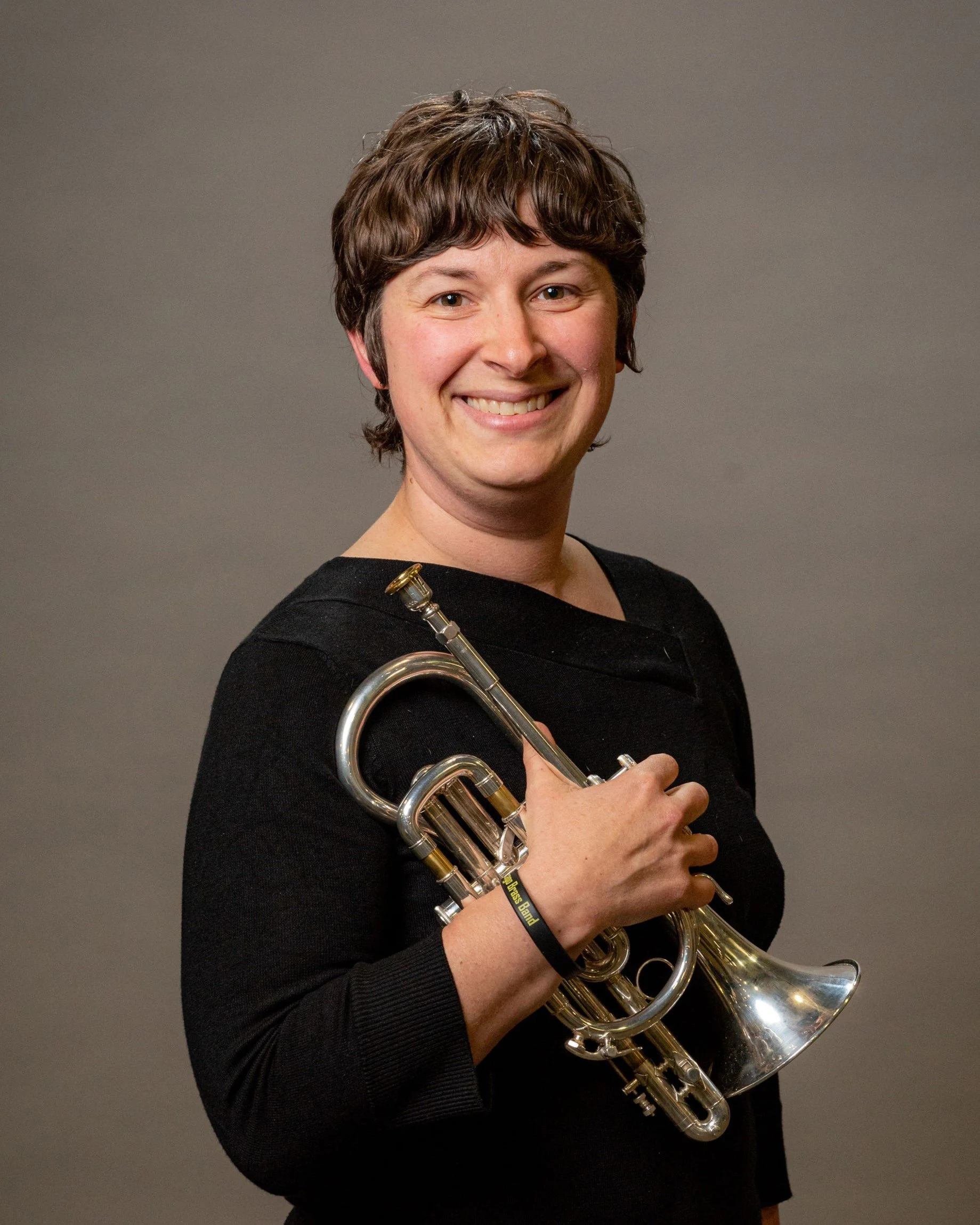 Smiling musician holding a silver French horn against a gray background