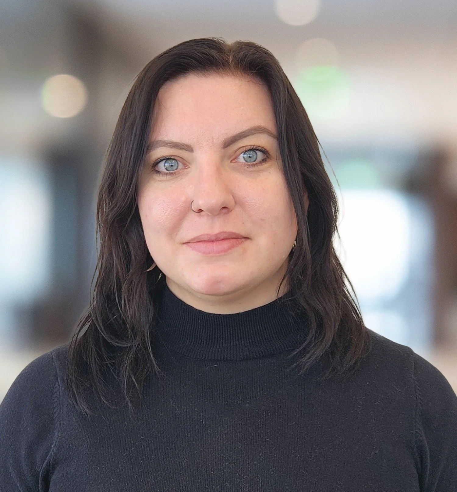 Portrait of a woman with dark hair, blue eyes, and a nose ring wearing a black sweater