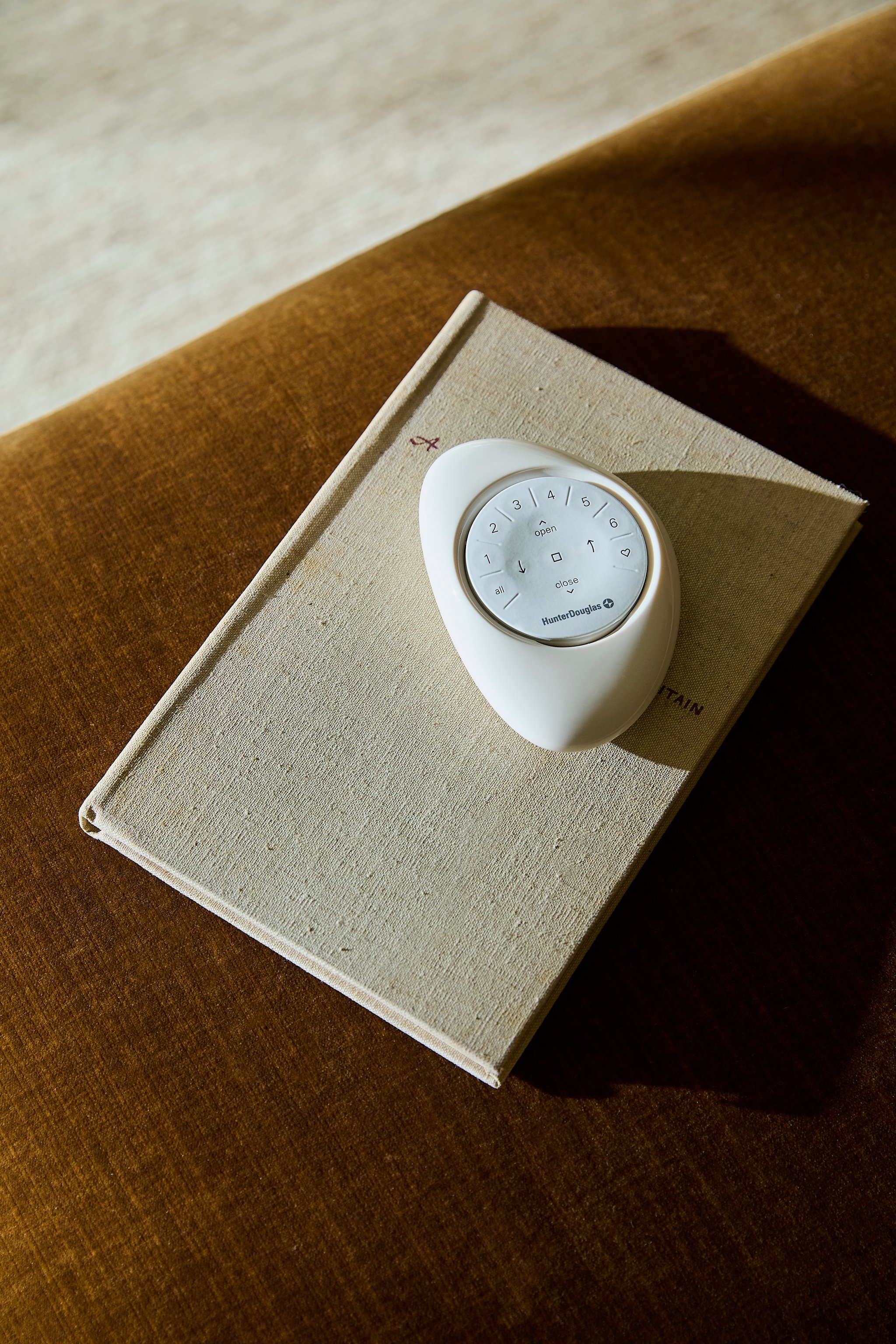 A remote control placed on top of a closed book on a brown fabric surface.