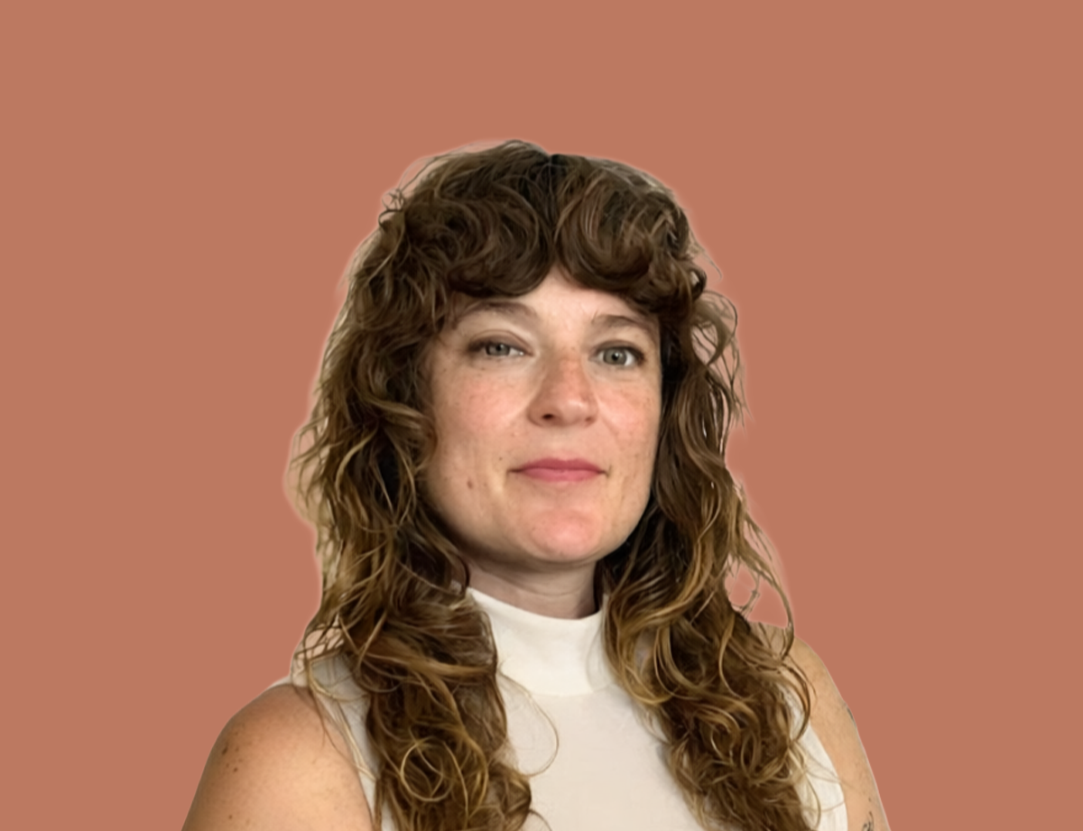 A woman with curly brown hair and fair skin, wearing a sleeveless white top, standing against a solid light brown background.