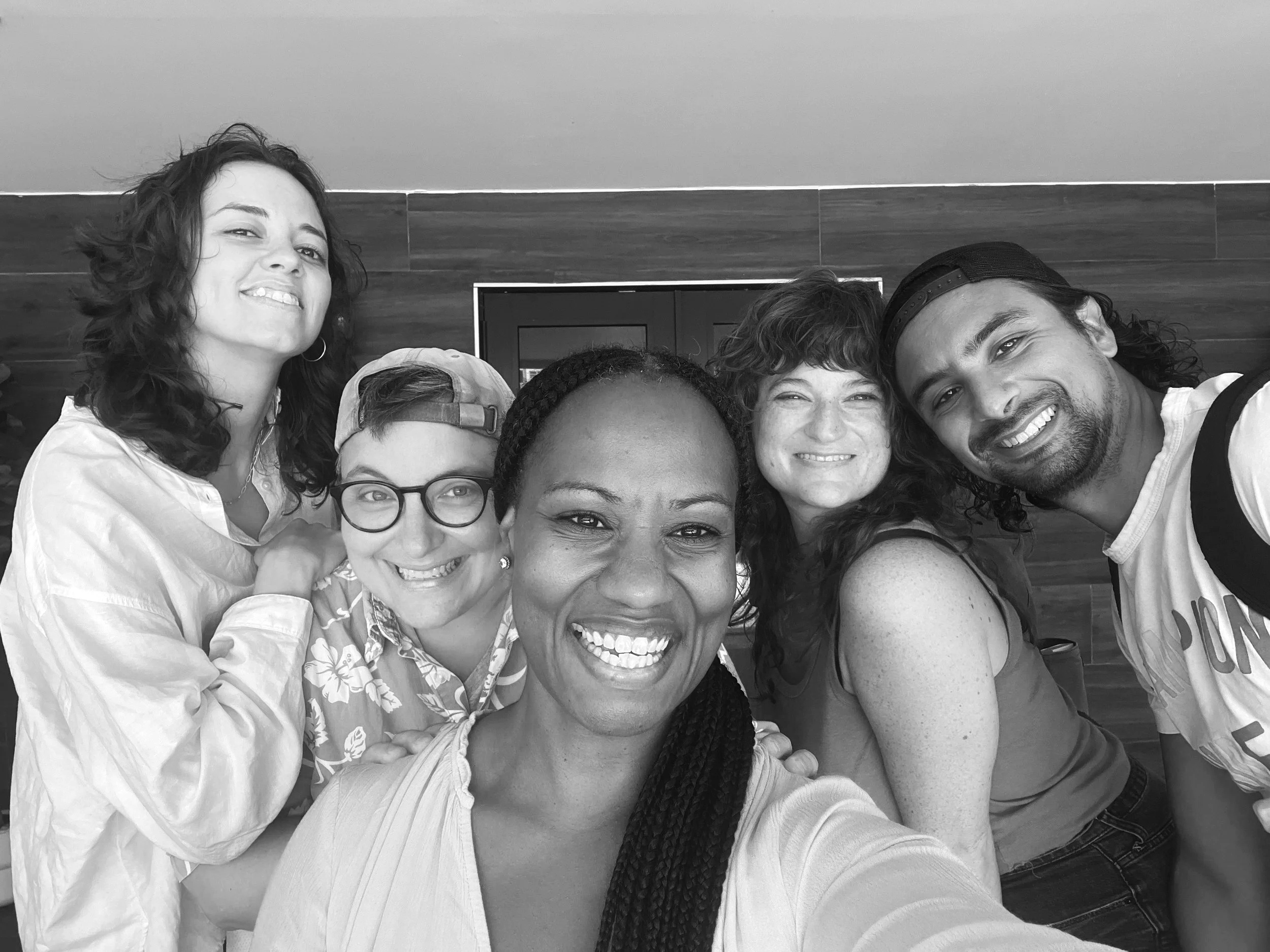 A group of diverse people smiling and taking a selfie indoors with wooden paneling on the wall behind them.