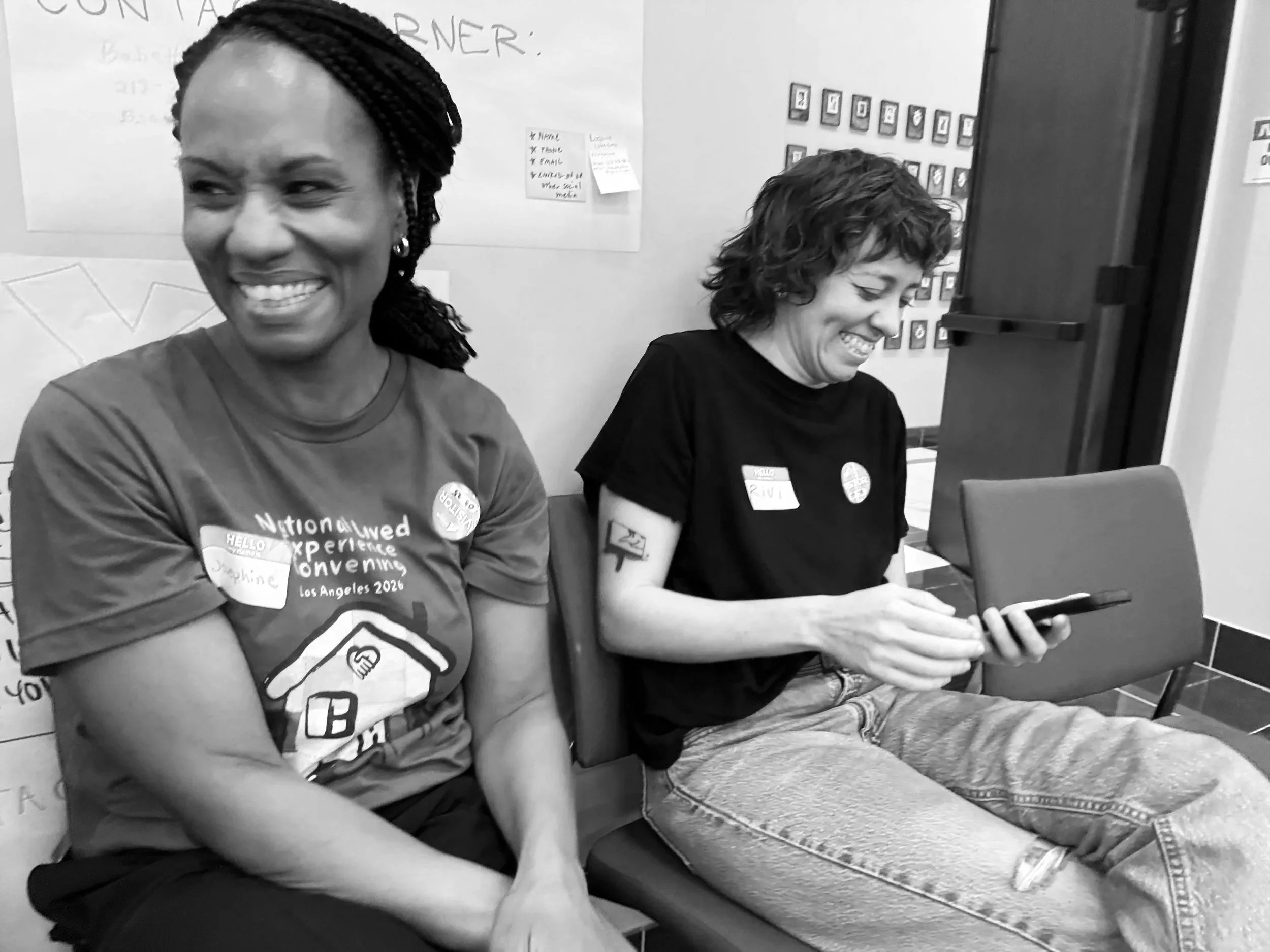 Two people sitting next to each other, laughing in a casual work environment.
