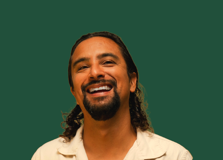Smiling man with long dark hair and a goatee, wearing a light-colored shirt, against a green background.