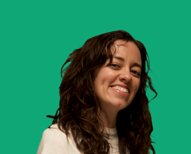 A person with curly brown hair smiling against a green background.