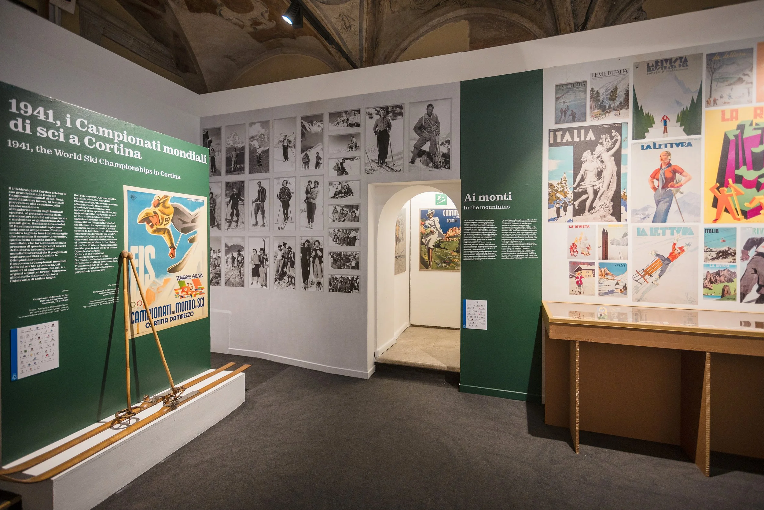 Mostra di fotografie storiche di sciatori e manifesti pubblicitari relativi ai Campionati mondiali di sci a Cortina d'Ampezzo nel 1941, con un'illustrazione di uno sciatore in primo piano.