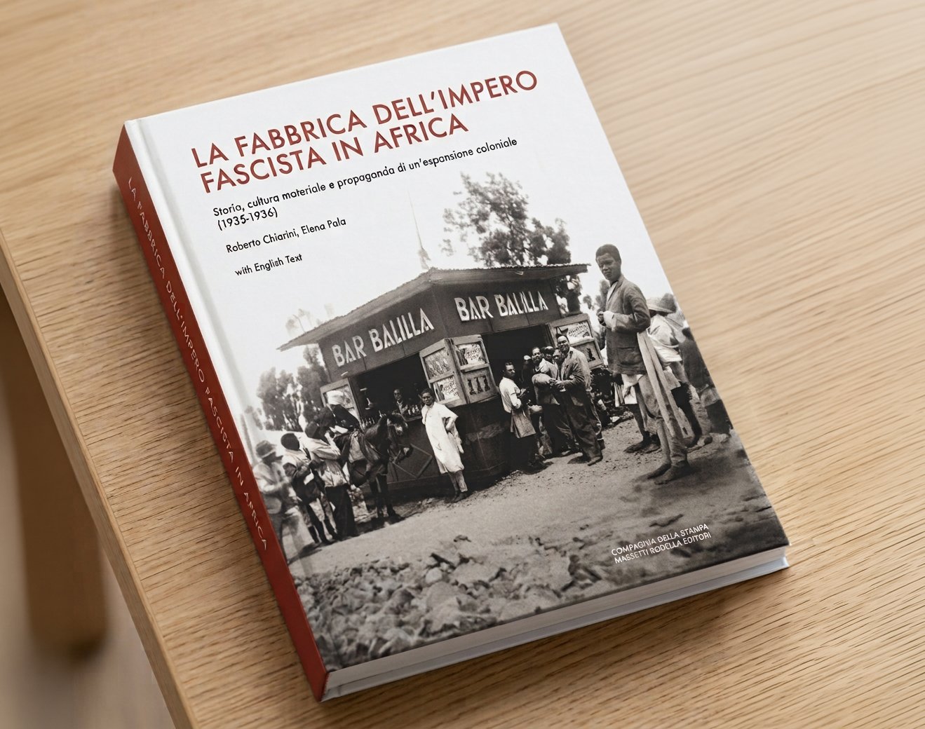 Libro intitolato "La fabbrica dell'impero fascista in Africa" con copertina che mostra una foto storica in bianco e nero di un gruppo di persone davanti a un chiosco con lo scritto "Bar Balilla".