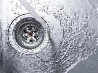 Water flowing into a drain with bubbles and ripples.