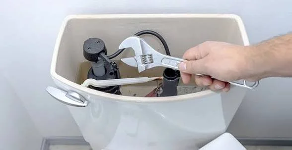 Person using wrench to turn a valve inside a toilet tank.