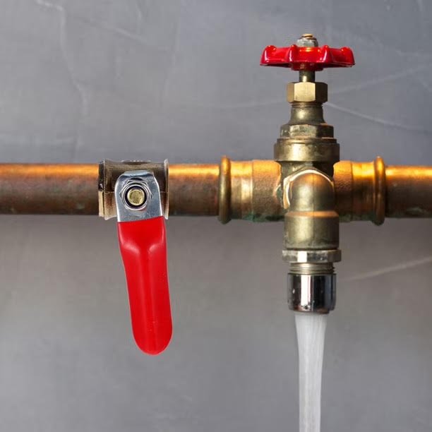 A brass plumbing valve with a red handle and a red knob, with water flowing out of the spout.