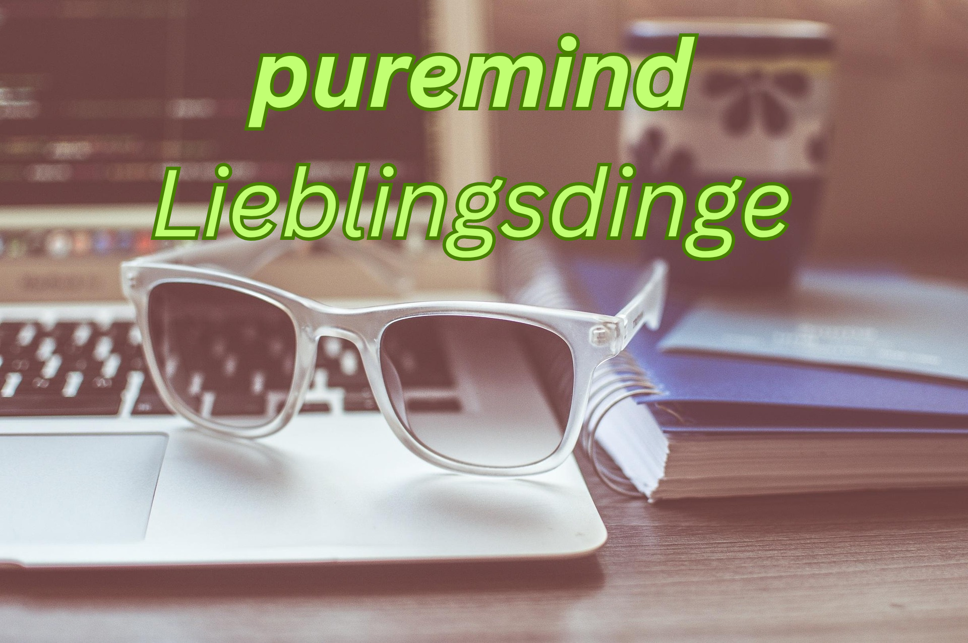 Blaue Sonnenbrille liegt auf einem offenen Laptop, im Hintergrund ein Notizbuch und ein Smartphone auf einem Holzschreibtisch, mit Text "puremind lieblingsdinge" in grün.