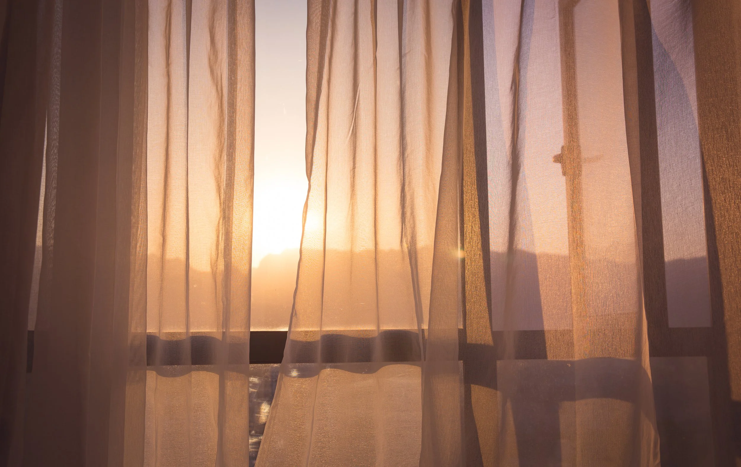 Sunlight shining through beige curtains at sunrise or sunset.