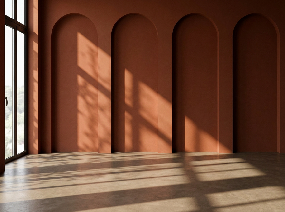 Empty room with pink walls and arched wall niches, sunlight casting shadows through large windows onto the floor.