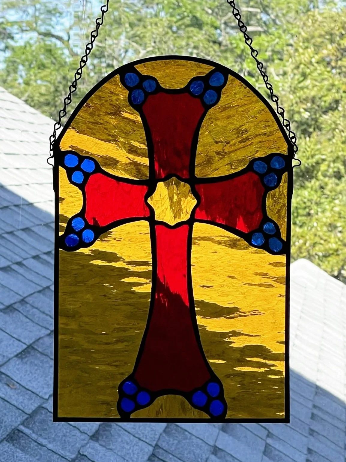 A stained glass window featuring a red cross with blue accents, set against a yellow background.