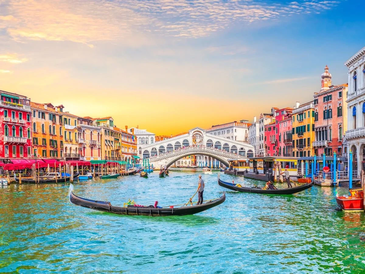 Vista del canal de Venecia con góndolas, edificios coloridos y el puente de los Suspiros al atardecer.