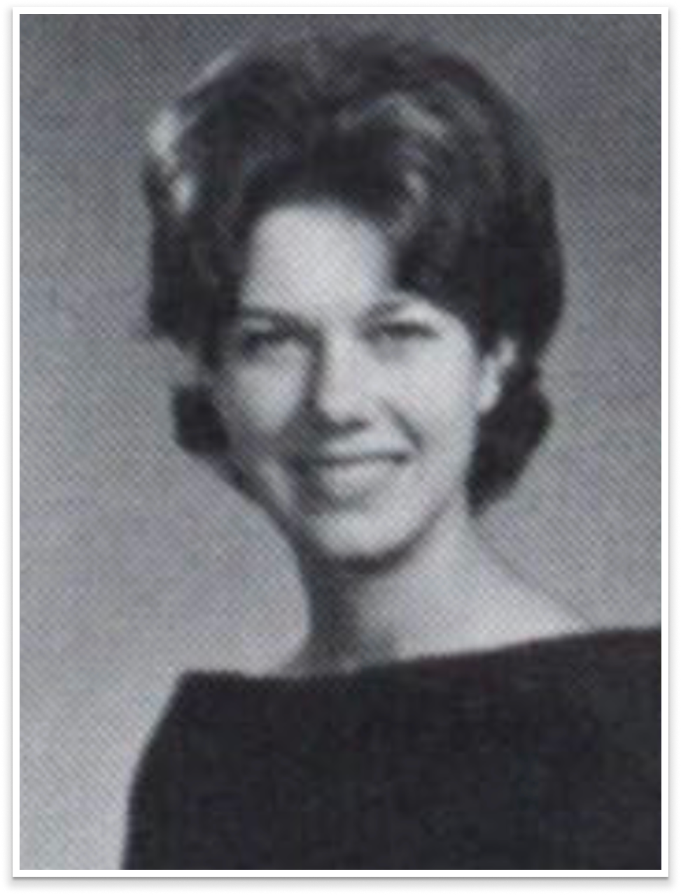 Black and white portrait of a smiling woman with short, styled hair, wearing a dark sleeveless top.