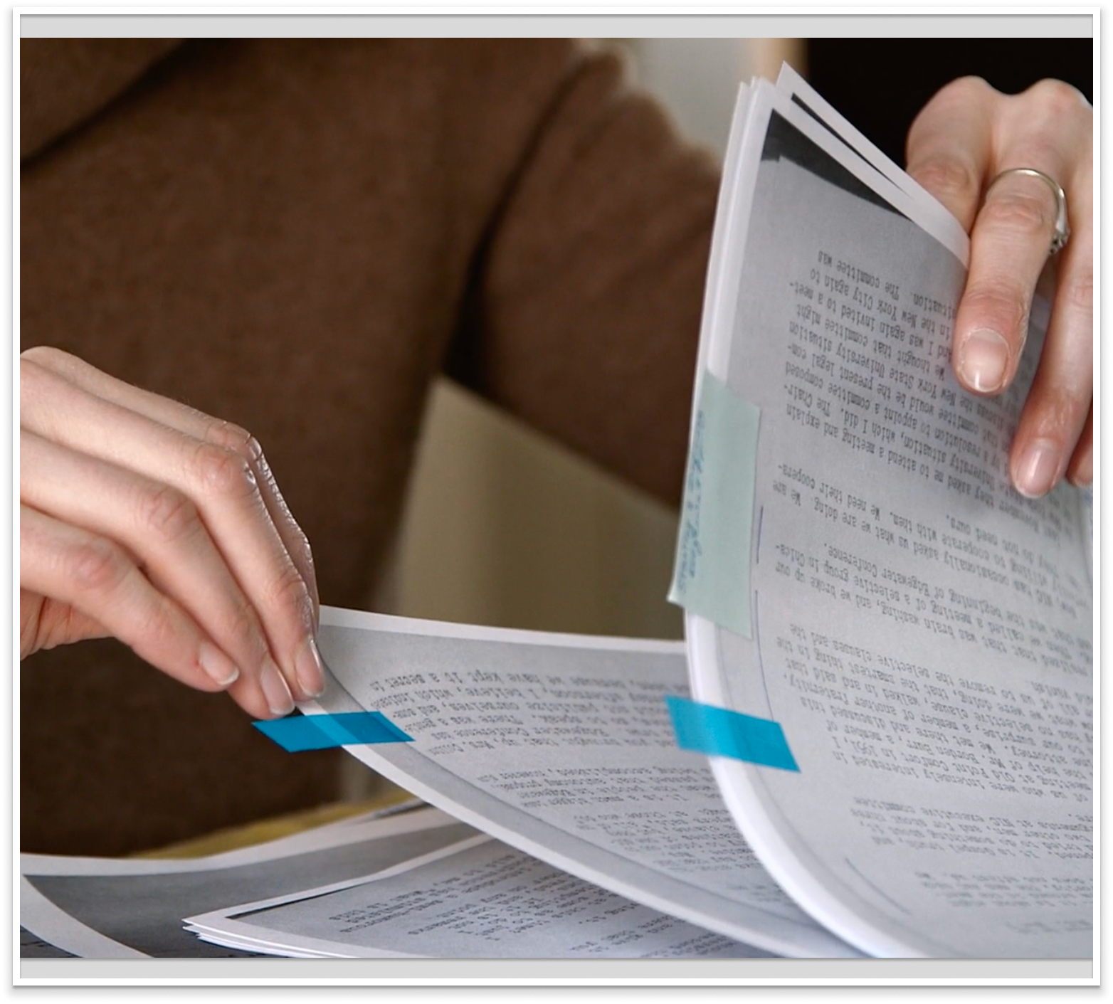 Close-up of a person's hands flipping through pages of documents, with some papers having blue tab markers.