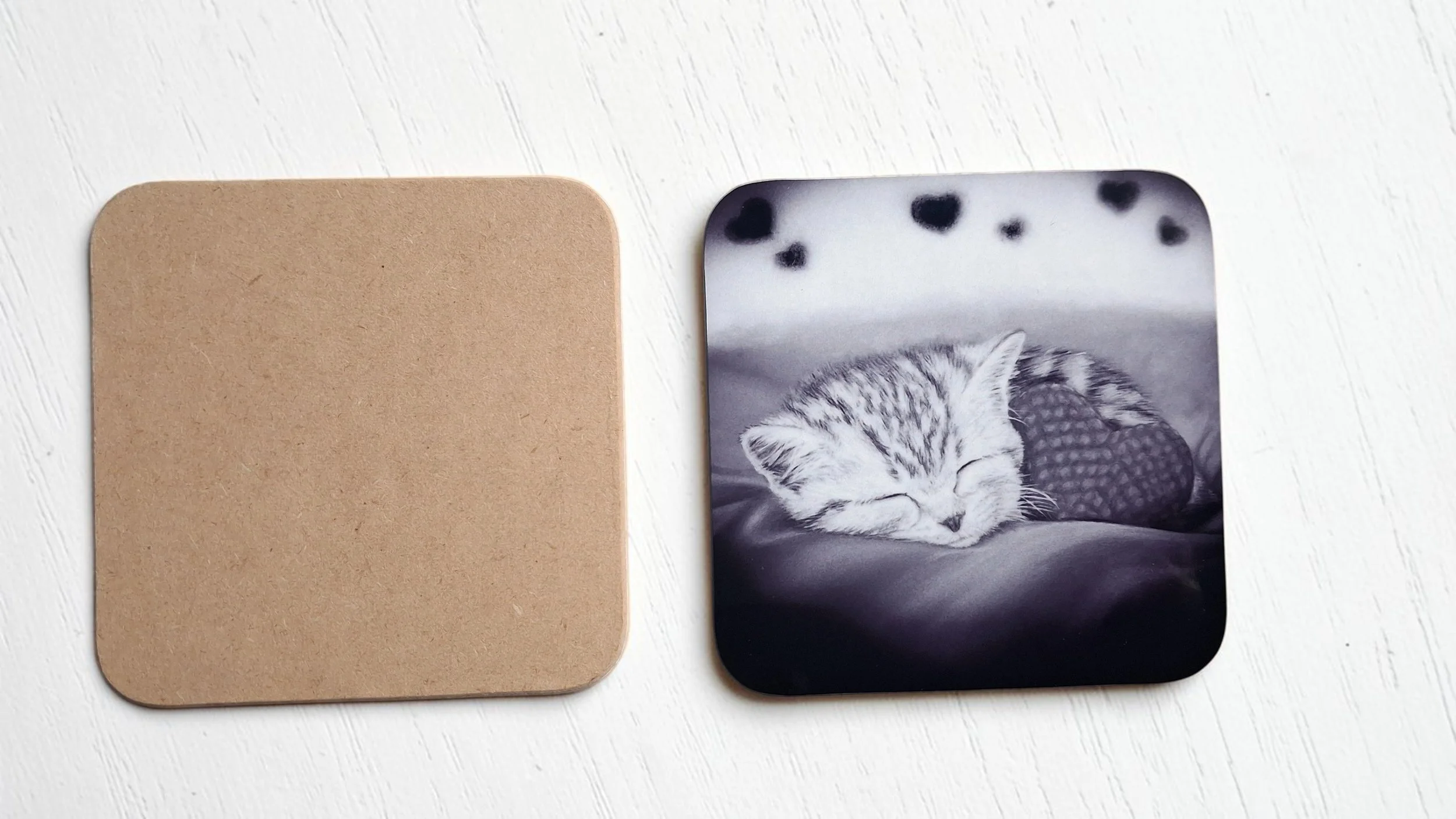 Two hardboard coasters with black and white glossy artwork of sleeping tabby kitten