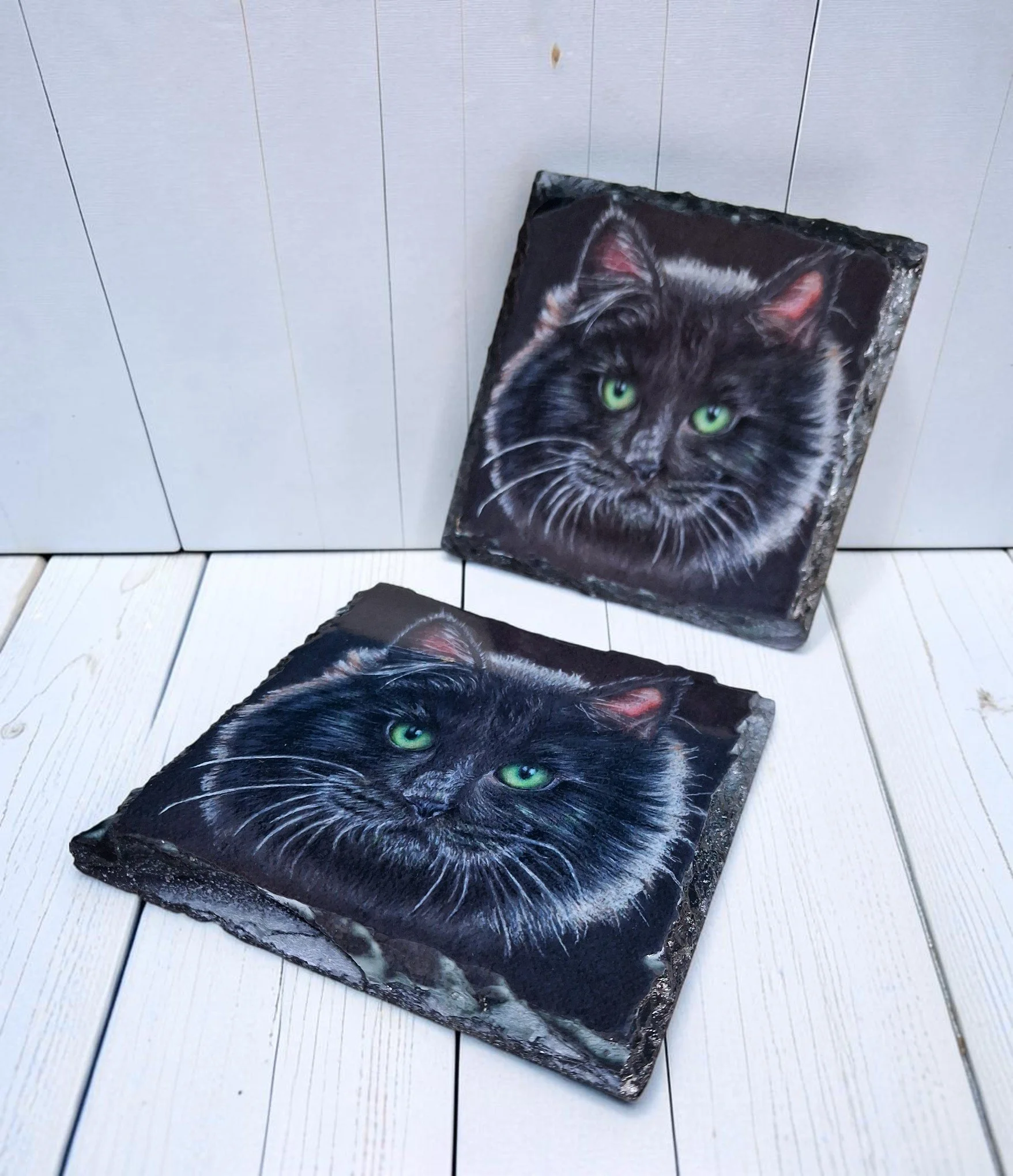 two slate coasters with artwork of black cat's face with green eyes