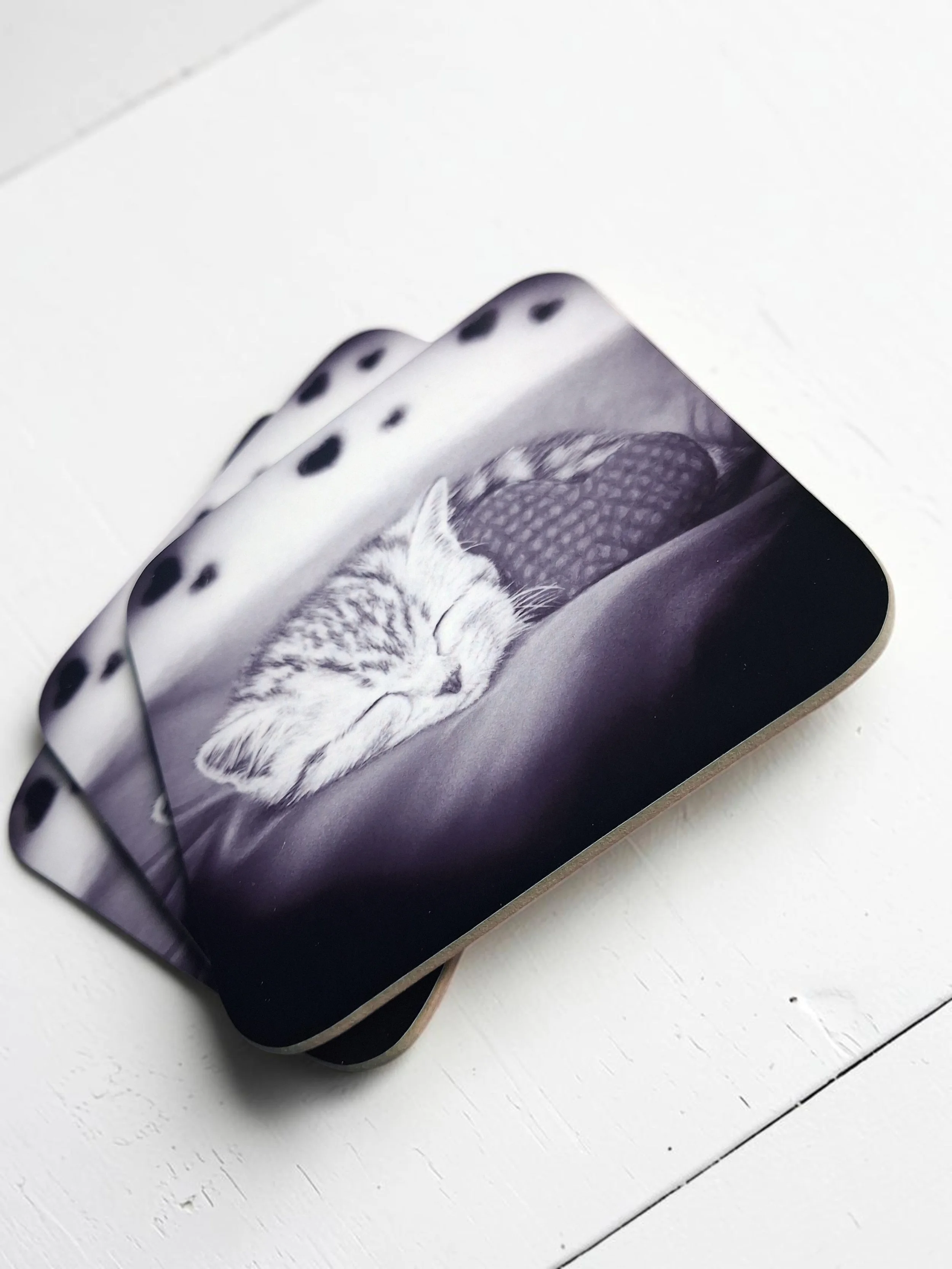 Hand drawn artwork printed onto hardboard coasters, in black and white glossy finish of a sleeping kitten snuggled up with a heart cushion