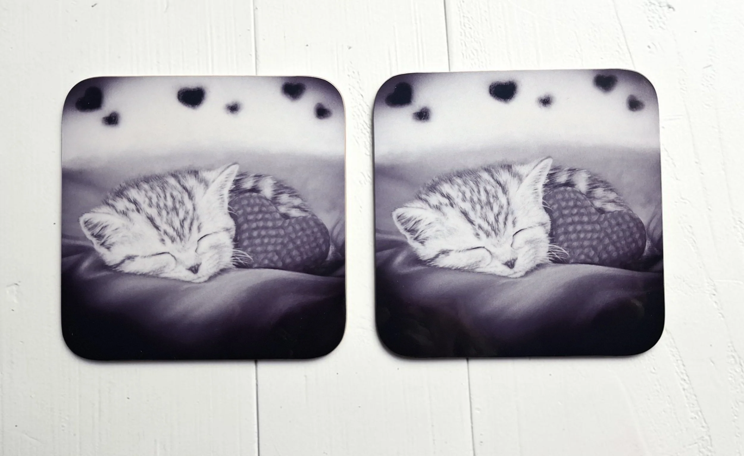 Two hardboard coasters with black and white glossy artwork of sleeping tabby kitten