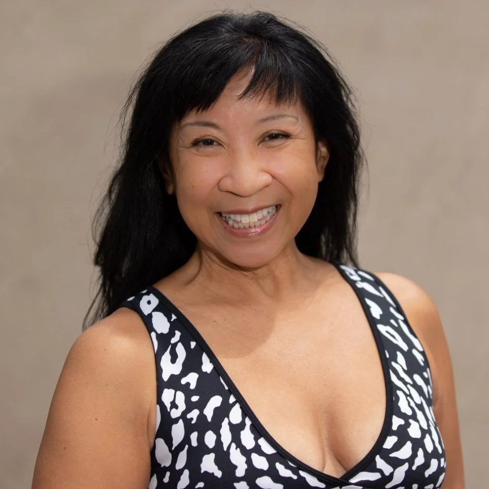 A woman with black hair smiling and wearing a black and white animal print sleeveless top.