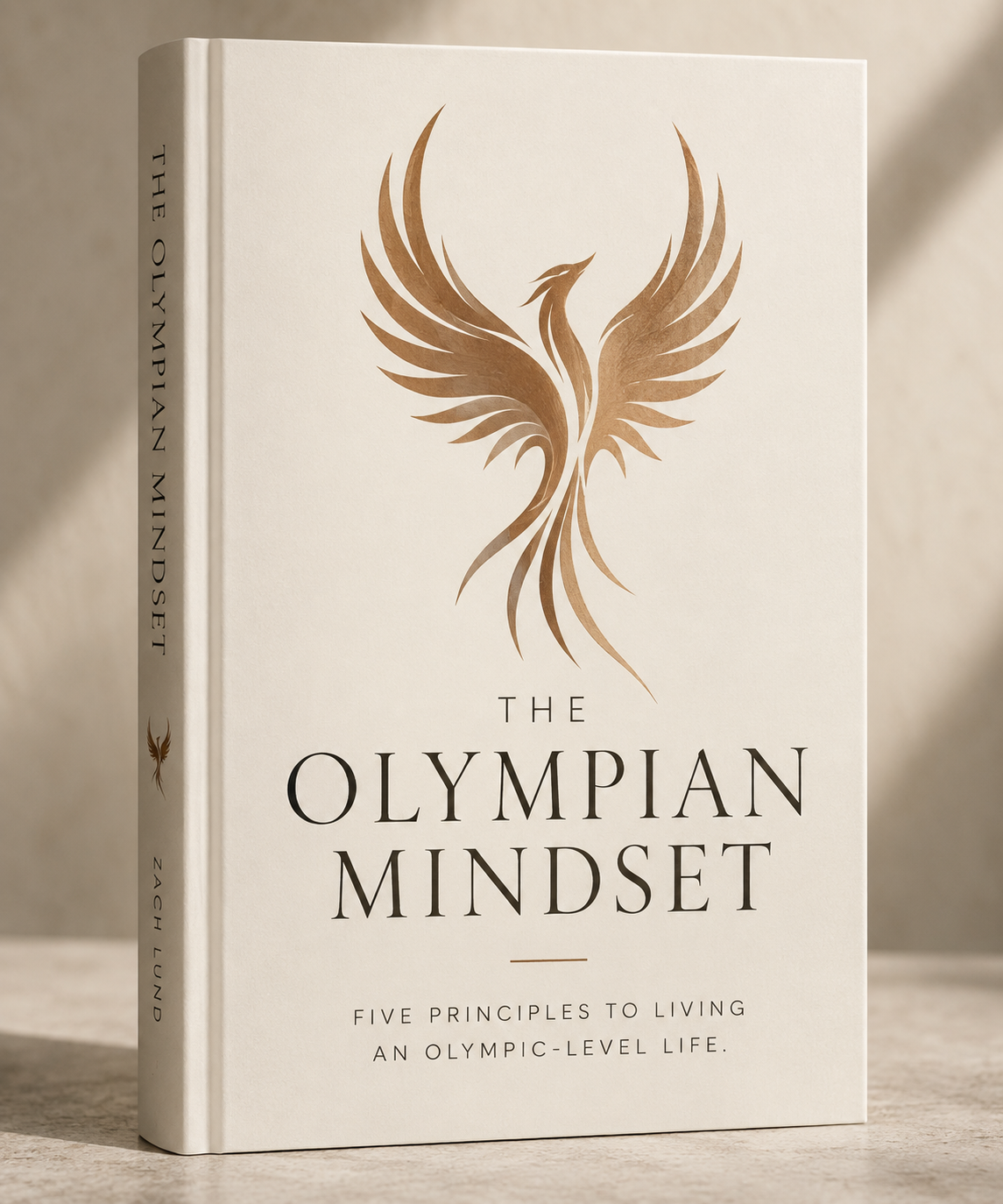 A book titled 'The Olympian Mindset' with a gold phoenix logo on the cover, standing on a light-colored surface with a neutral background.