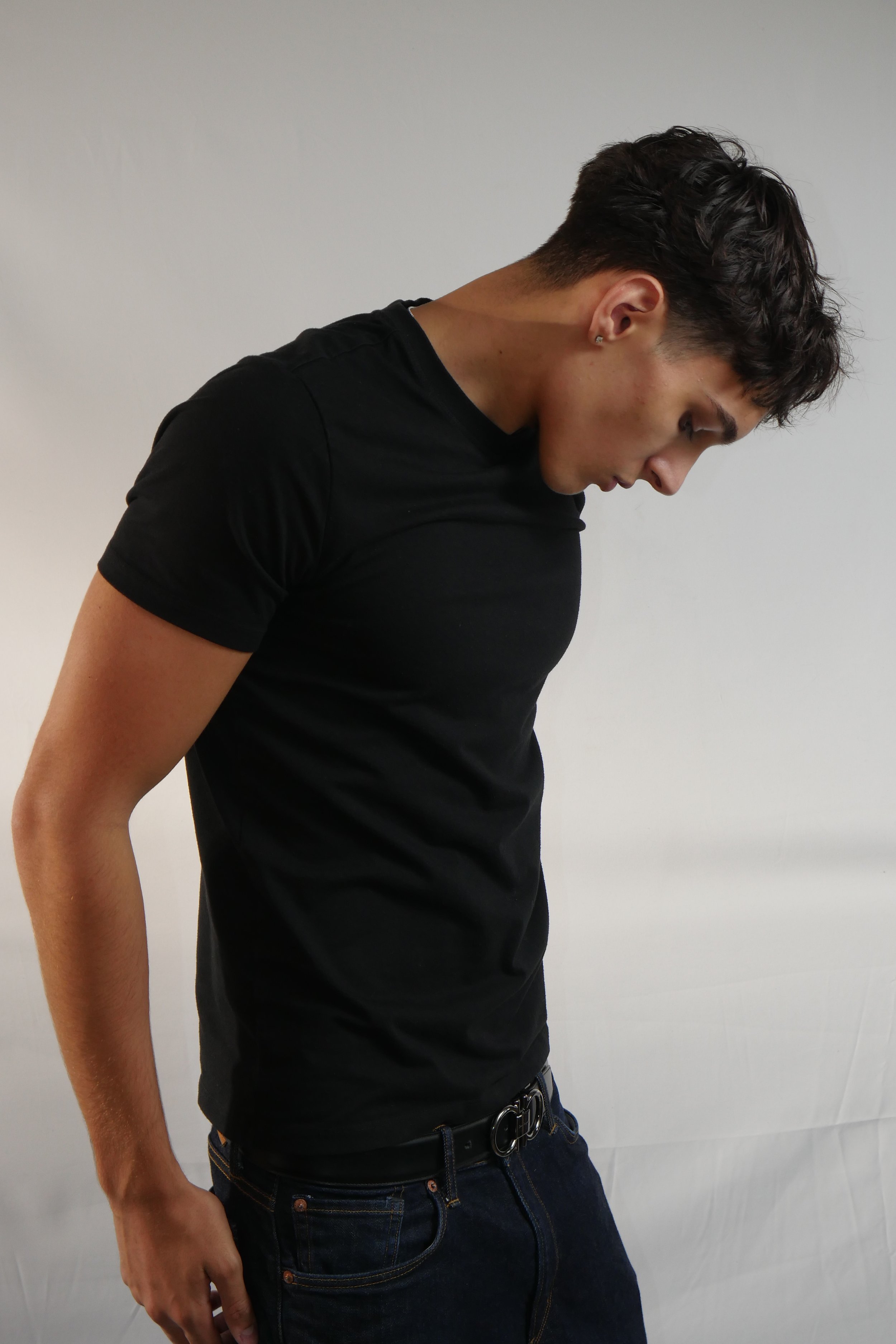 Jeune homme debout, portant un t-shirt noir et un jean, dans un fond gris