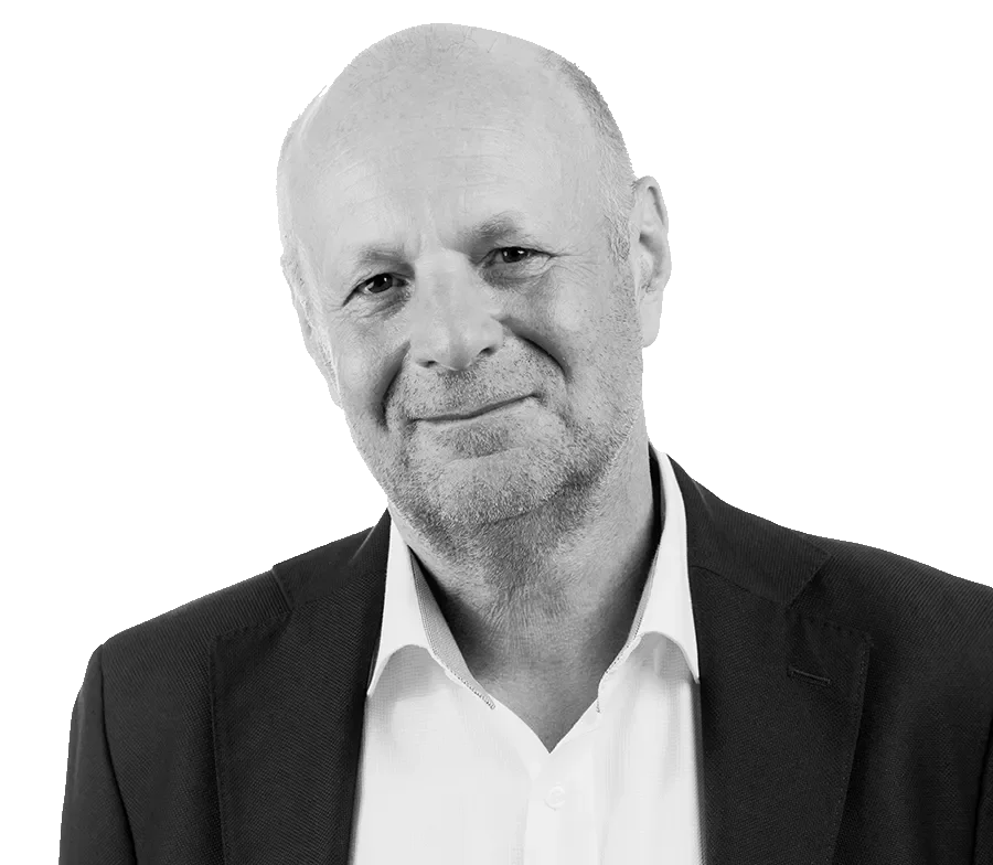 A black and white portrait of an older man with short hair and a beard, wearing a dark blazer and a white shirt.