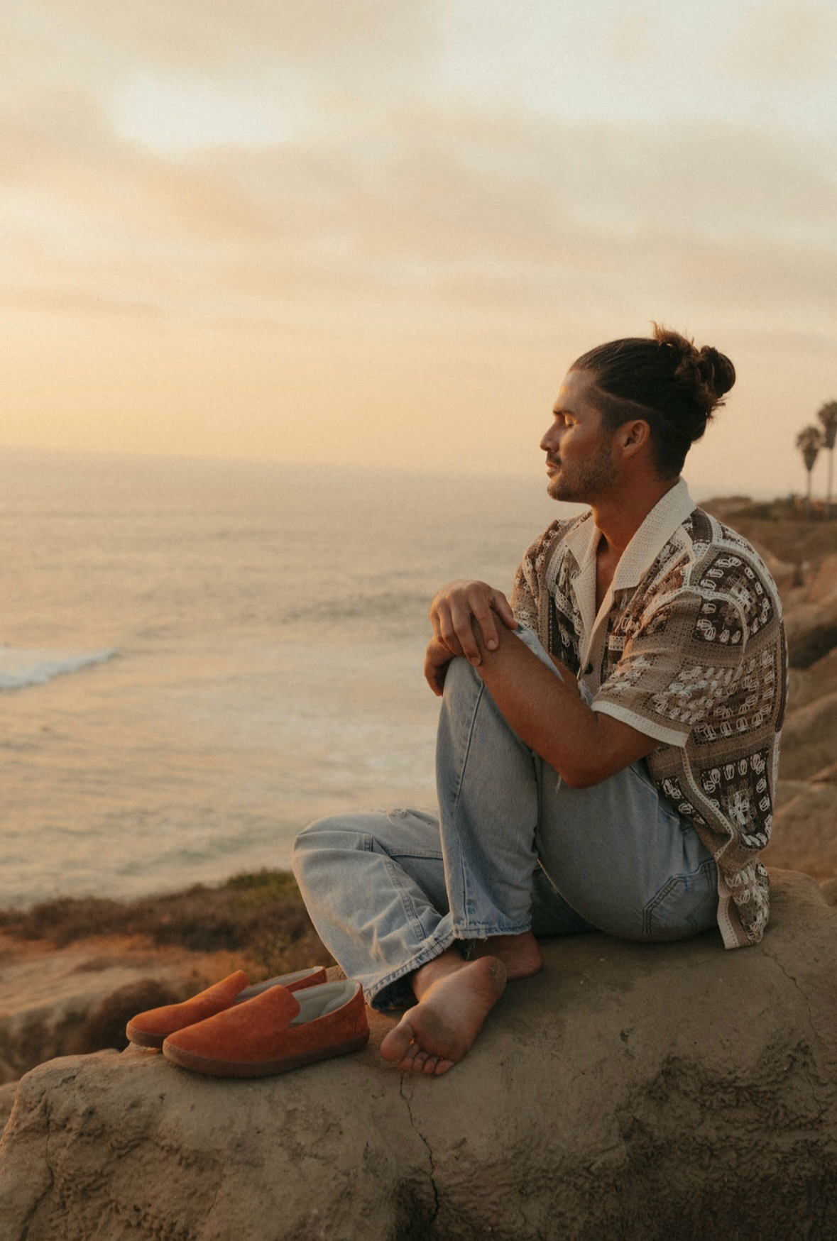Taylor Garrison sitting on cliff overlooking beach in a meditative pose, taking a breath and regulating his nervous system