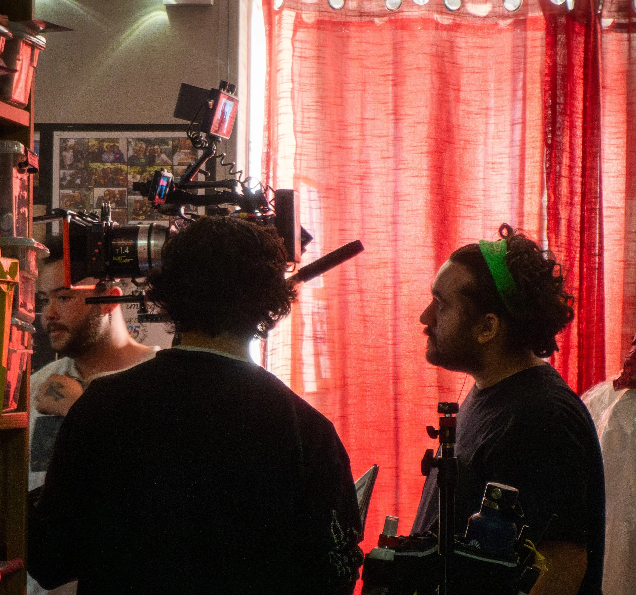Inside a video production or streaming setup with multiple cameras, monitors, and equipment, with a red curtain in the background.