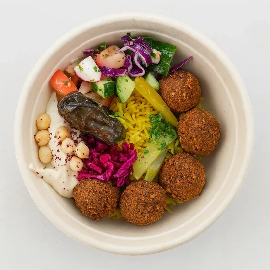 Bowl of Mediterranean food with falafel, cucumber, tomato, paprika, pickles, white beans, yogurt, and salad.