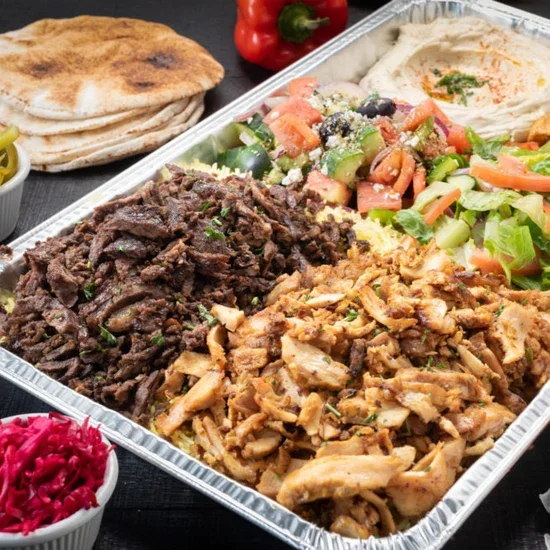 A large aluminum tray filled with Mexican food, including shredded beef, shredded chicken, fresh salad with tomatoes, cucumbers, black olives, and shredded cheese, accompanied by tortillas, a small bowl of pickled red cabbage, and a red bell pepper.