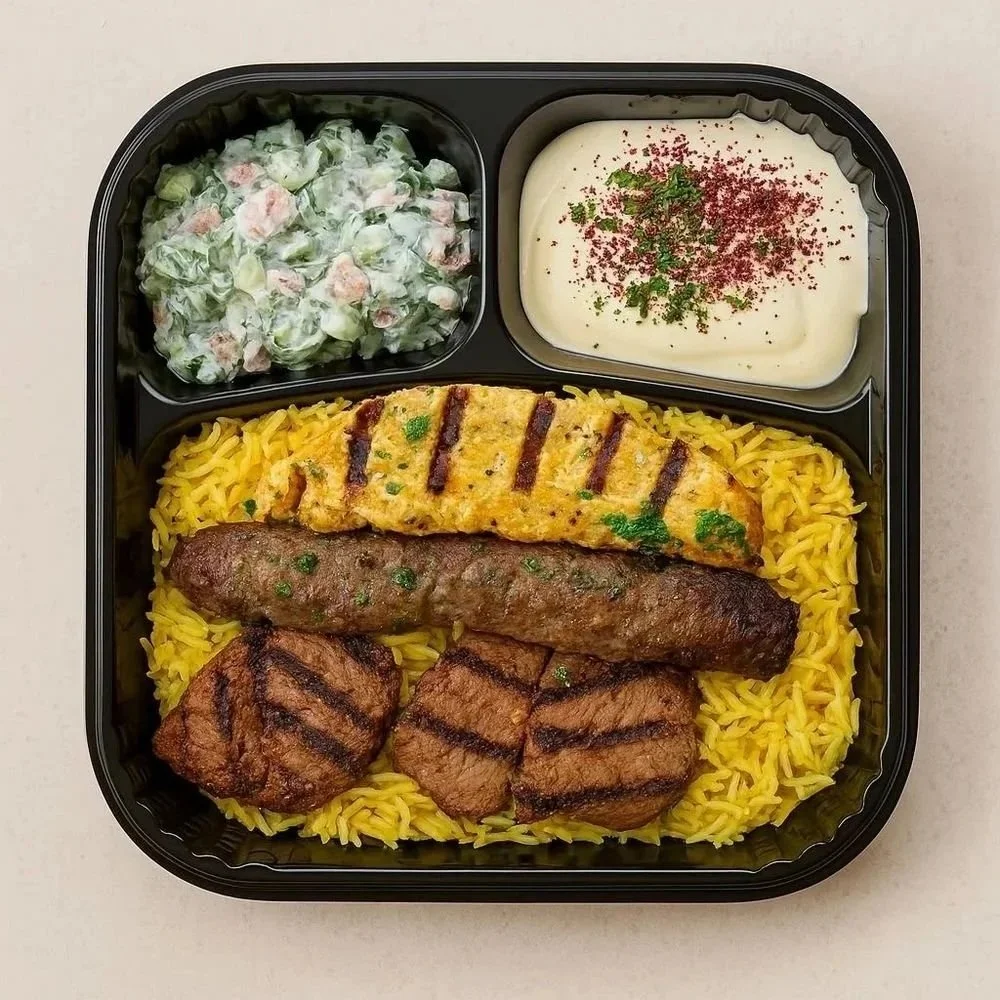A meal in a black compartmentalized tray with yellow rice, grilled meat, a grilled chicken patty, a Turkish sausage, a side salad with creamy dressing, and a dish of white sauce garnished with red spice and green herbs.