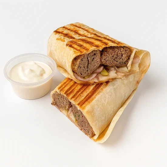 Grilled wrap sandwich with sliced beef, onions, and pickles, served with a side of ranch dressing.