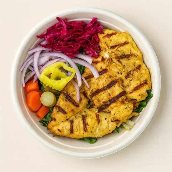 Grilled chicken breast on a bed of greens with sliced onions, pickles, shredded red cabbage, shredded carrots, and cherry tomatoes in a bowl.