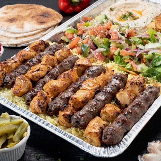 A tray of grilled kebabs with rice, served with salad, pita bread, a fried egg, and pickles.